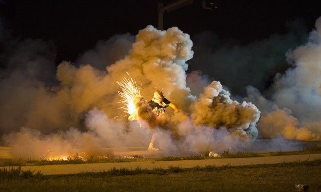 A protester throws back a smoke bomb while clashing with police in Ferguson, Missouri